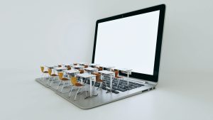 Miniature school desks on a laptop keyboard to symbolize online learning